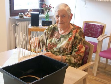 Seniorin am Tisch beim Korbflechten