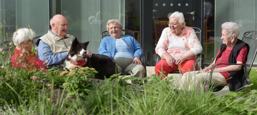Fünf Senioren mit Hund sitzen zusammen im Garten