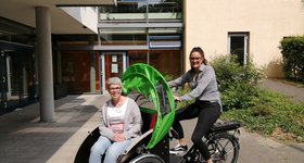 Eine Frau sitzt auf einer Fahrradrikscha. Eine jüngere Frau sitzt auf dem Sattel.