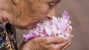 ältere Dame riecht an Blume