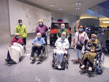 Betagte Besuchergruppe in Rollstühlen vor Autos im Museum