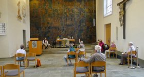 Senioren sitzen im Kirchenraum auf Stühlen und lauschen