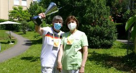 2 Mitarbeiterinnen mit Maske und Dienstkleidung halten Pokal hoch