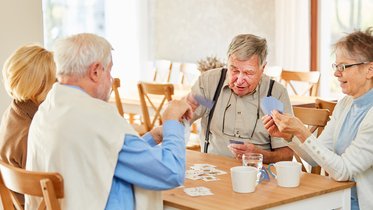 Vier Seniorinnen und Senioren sitzen gemeinsam am Tisch und spielen Karten.