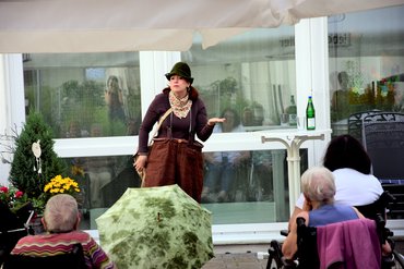 Frau mit Jägerhut und brauner Clownshose performt vor Publikum