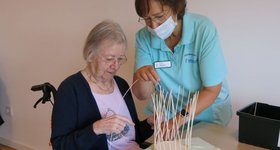 Betreuerin unterstützt Seniorin beim Korbflechten